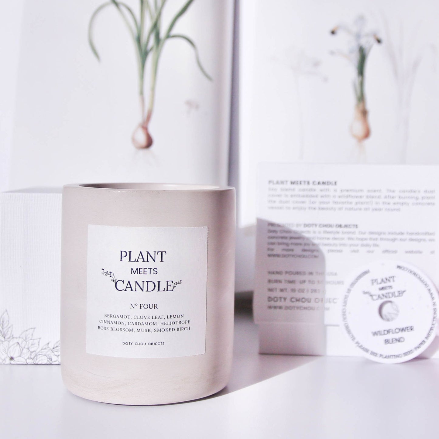 A light grey concrete vessel containing Plant Meets Candle No. Five displayed with botanical images alongside its product box and seed paper dustcover.